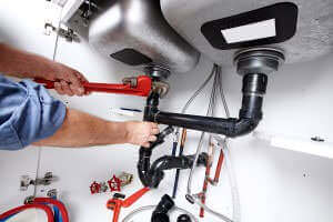 A plumber repairing a drain pipe under a sink